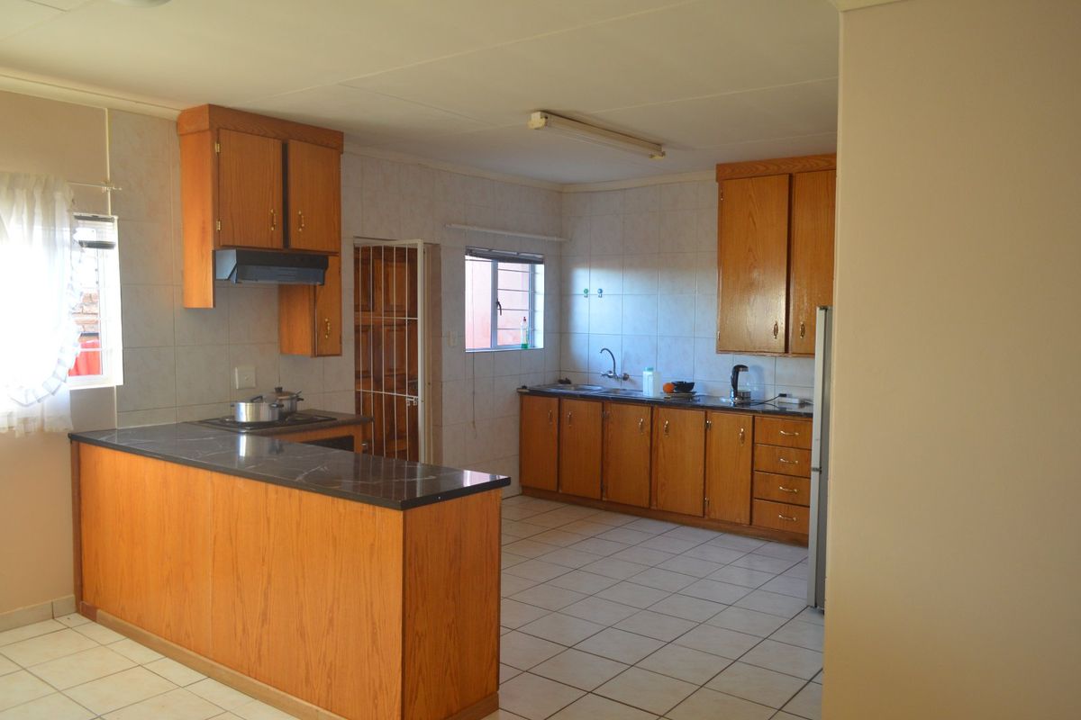 A functional kitchen featuring wooden cabinetry, laminate countertops, tiled walls, and a breakfast bar, offering a classic layout with potential for modern updates.