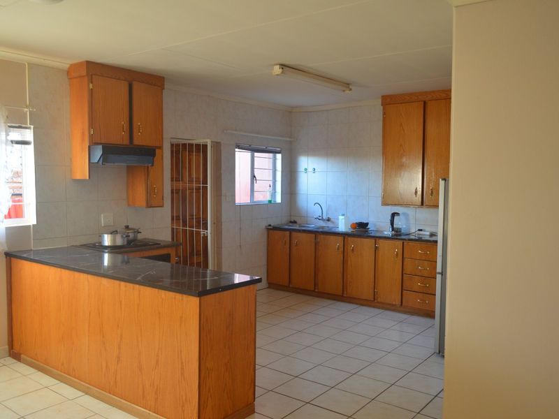A functional kitchen featuring wooden cabinetry, laminate countertops, tiled walls, and a breakfast bar, offering a classic layout with potential for modern updates.
