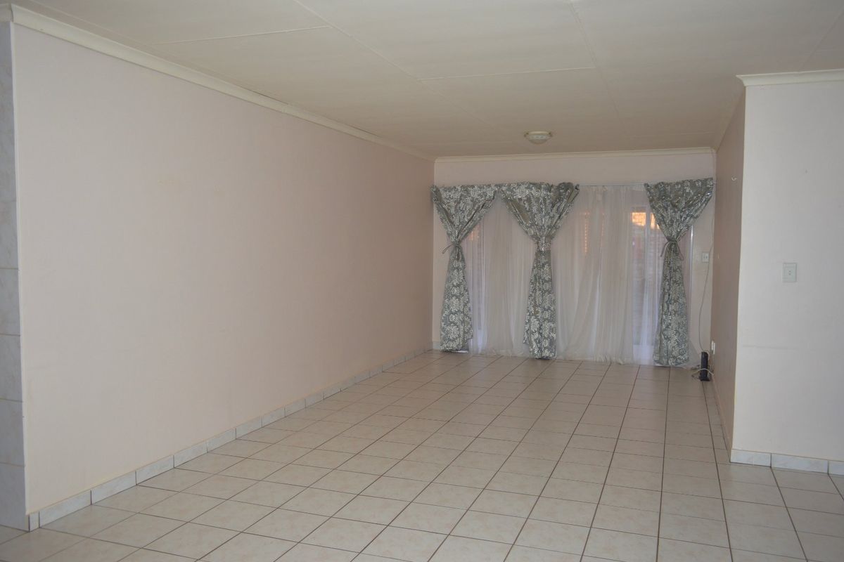 A spacious, empty living room featuring neutral tiled flooring, coved ceilings, and a large sliding glass door providing access to the exterior.