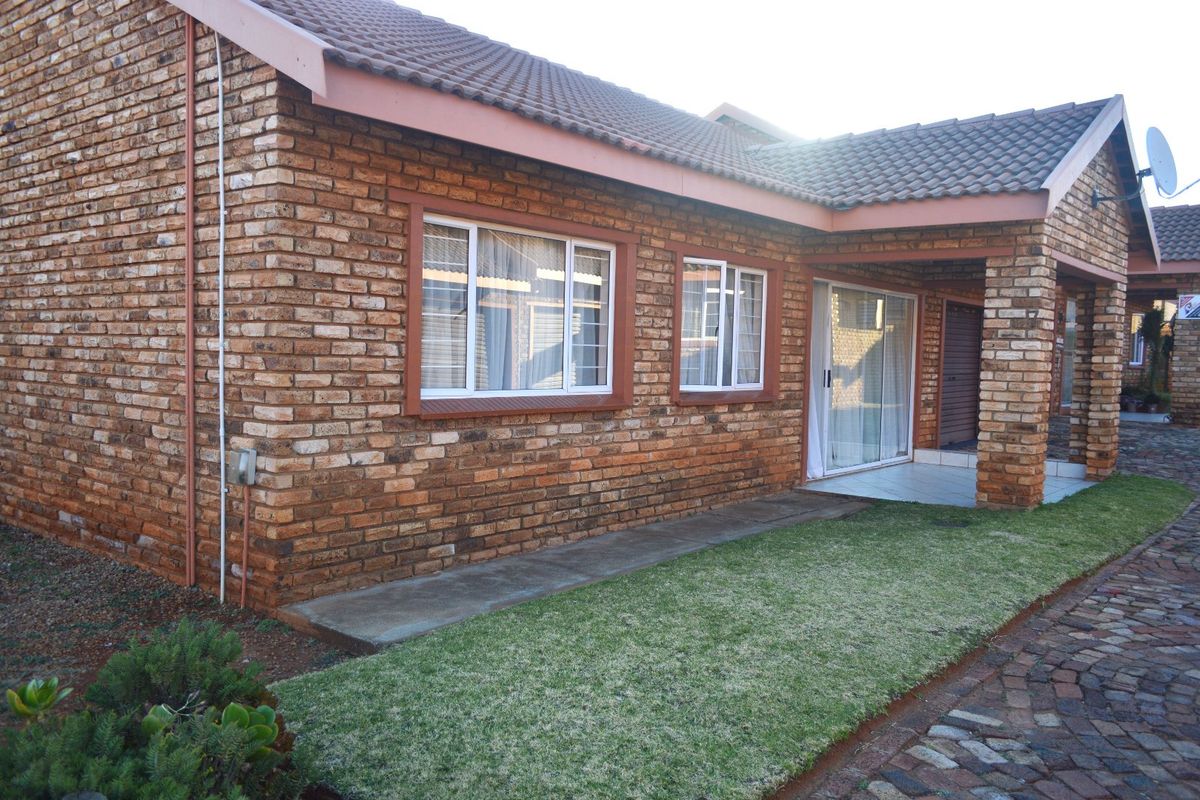 A well-maintained townhouse exterior featuring face brick construction, a tiled roof, aluminium window frames, and a neat garden area with a paved walkway.