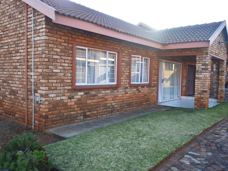 A well-maintained townhouse exterior featuring face brick construction, a tiled roof, aluminium window frames, and a neat garden area with a paved walkway.