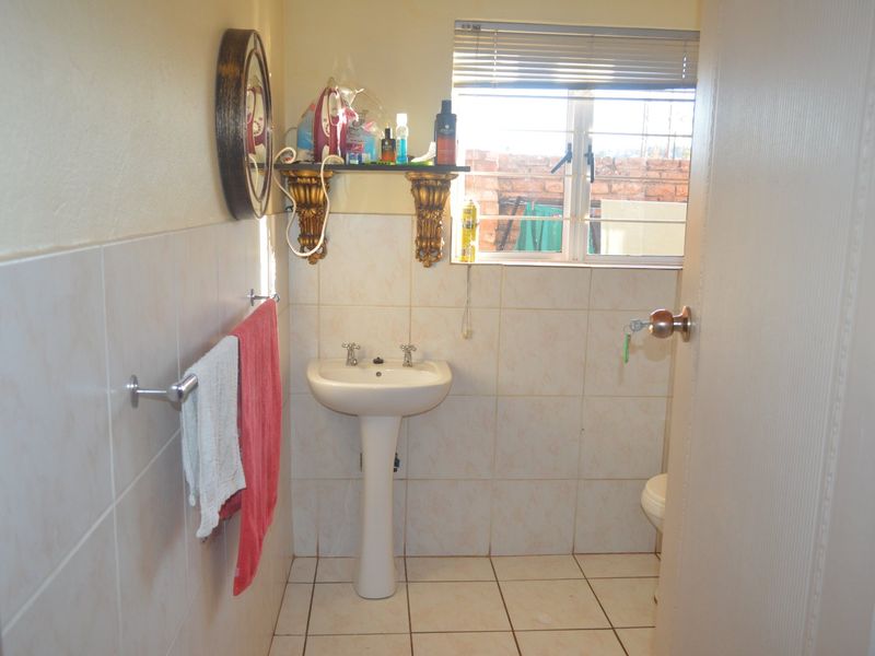 A functional bathroom featuring a pedestal basin, tiled walls and flooring, and a window with security bars.
