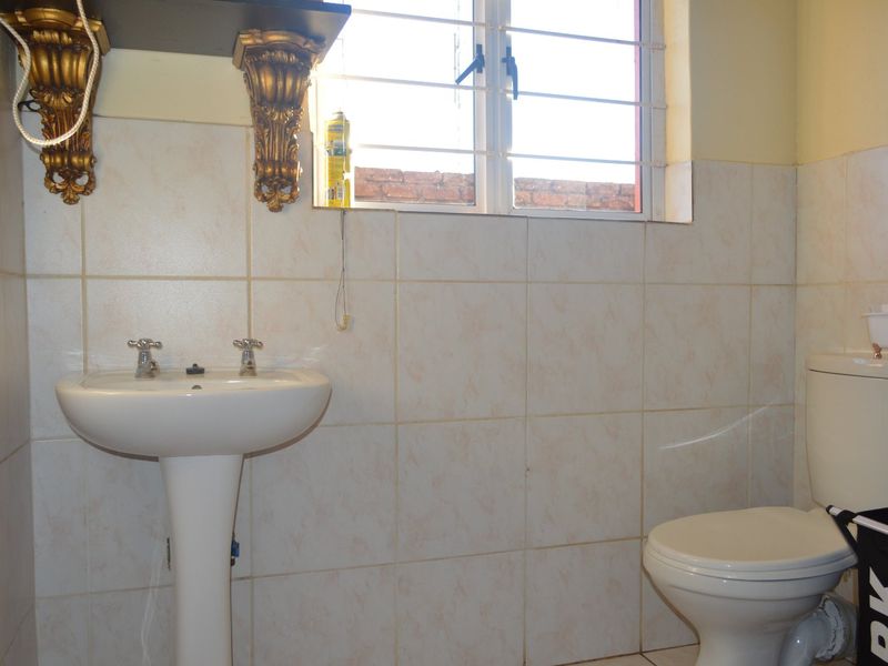 A functional bathroom featuring a pedestal basin, toilet, and tiled walls with security bars on the window.
