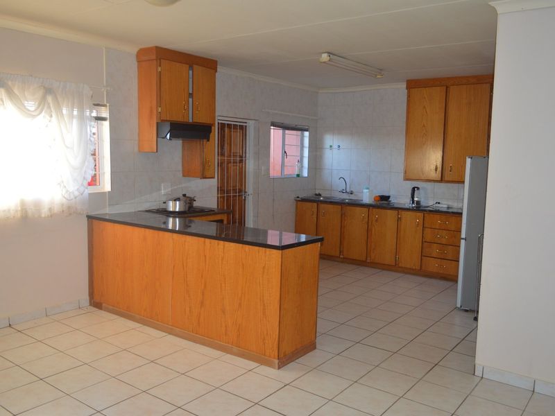A functional kitchen featuring wooden cabinetry, laminate countertops, tiled flooring, and wall tiling, offering a practical layout with a breakfast bar.