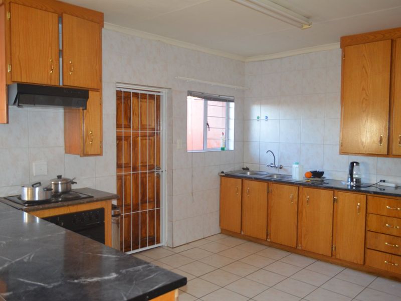 Functional kitchen featuring wooden cabinetry, laminate countertops, built-in oven and hob, tiled splashbacks, and direct access to an exterior door.