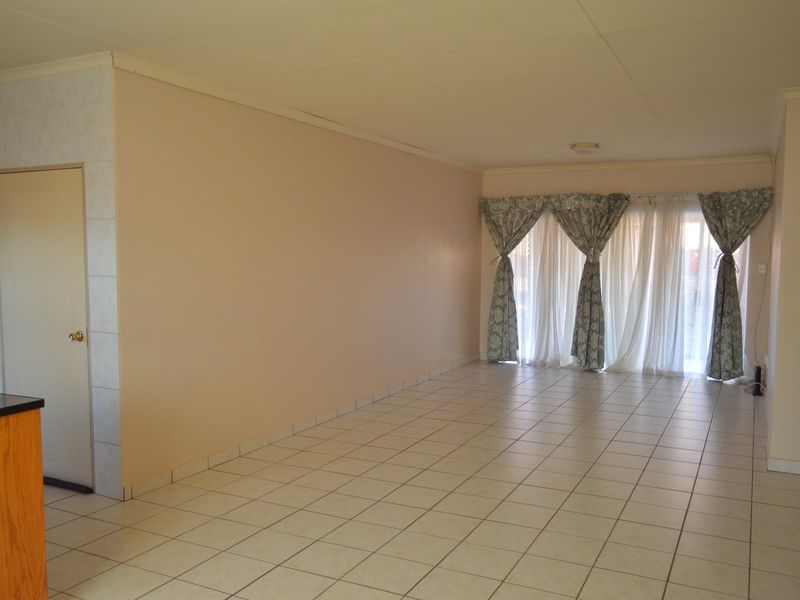 Spacious open-plan living area featuring neutral tiled flooring, coved ceilings, and a large sliding glass door providing natural light.