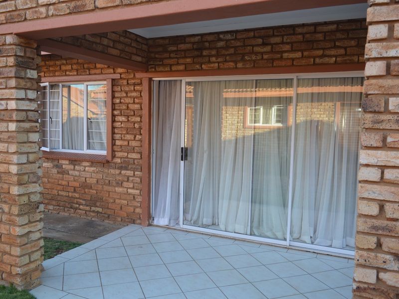 A covered patio area featuring exposed brick walls, tiled flooring, and large sliding glass doors providing access to the interior living space.