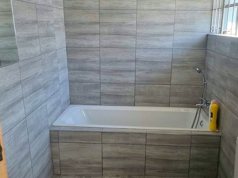 A modern bathroom featuring full-height wood-look wall tiling, a built-in bathtub with a handheld shower mixer, and a standard toilet.