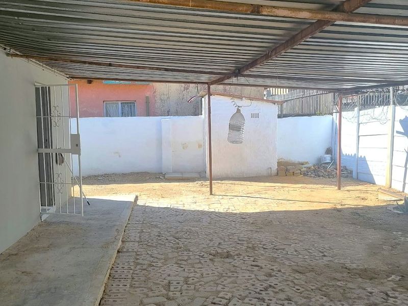 A covered outdoor patio area featuring a corrugated metal roof, concrete paving, and perimeter walling, providing a functional space for outdoor use.