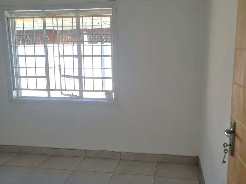 A vacant bedroom featuring neutral tiled flooring, white walls, and a window fitted with security bars.