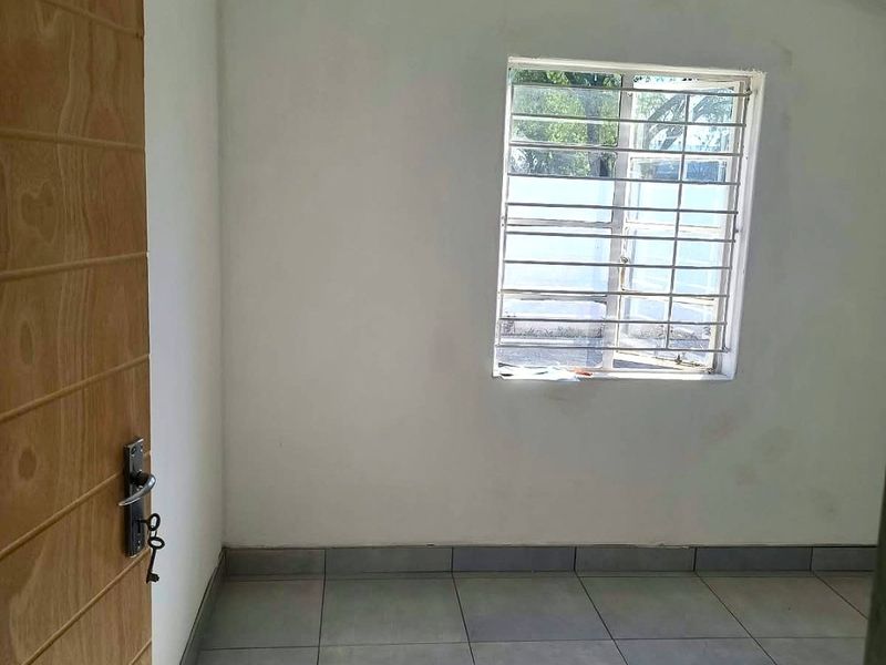 An empty bedroom featuring tiled flooring, a vaulted ceiling, and a window fitted with security bars.