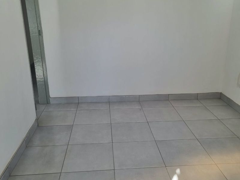 A clean, empty room featuring neutral ceramic floor tiles and white walls, providing a versatile blank canvas for any interior design style.