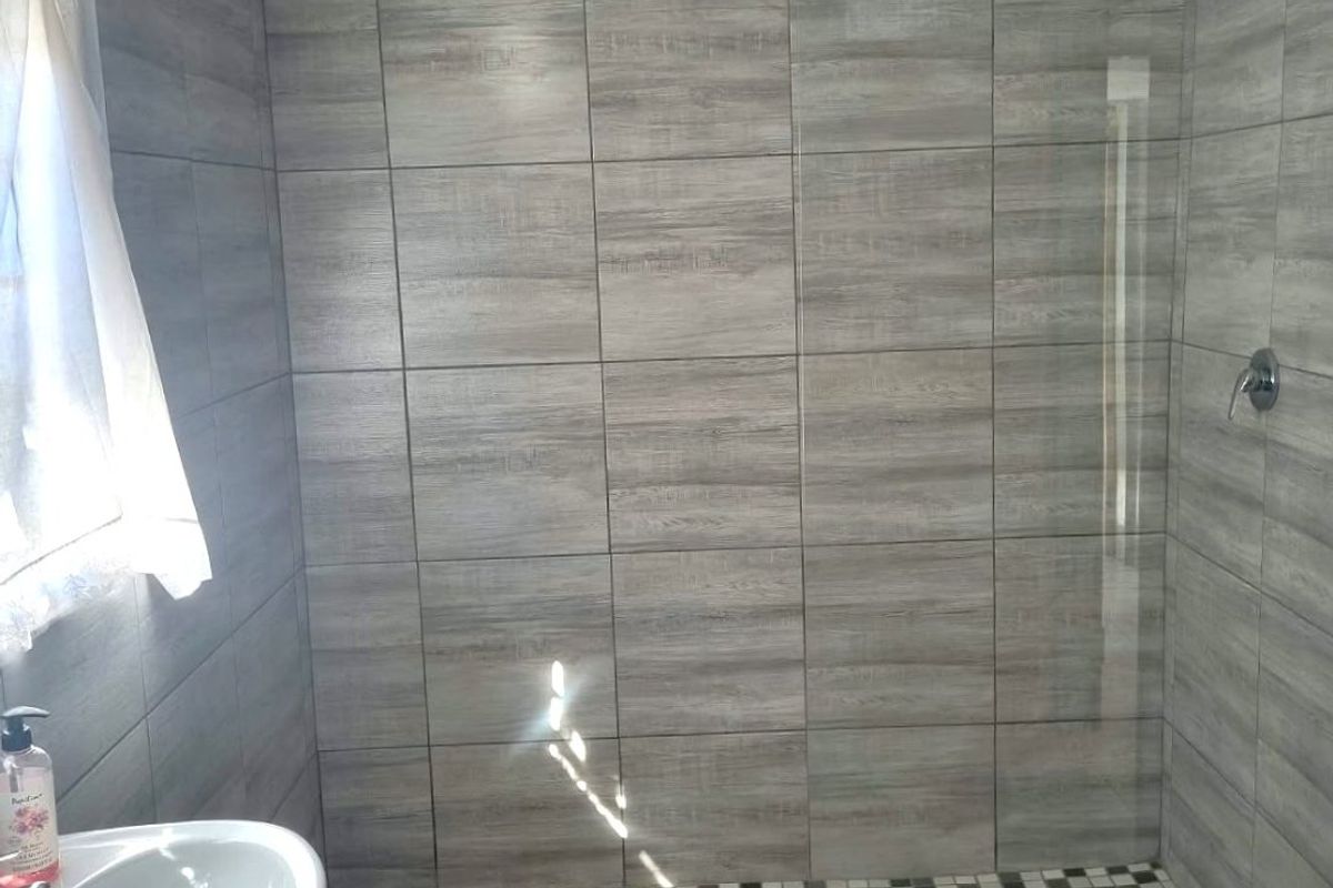 Modern bathroom featuring a walk-in shower with glass screen, wood-look wall tiles, and a pedestal basin.