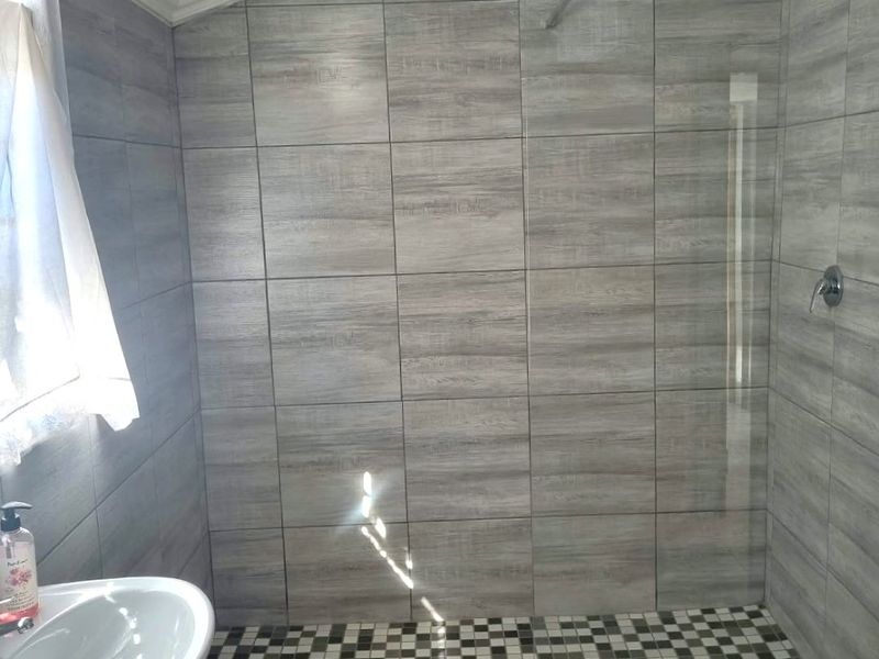 Modern bathroom featuring a walk-in shower with glass screen, wood-look wall tiles, and a pedestal basin.