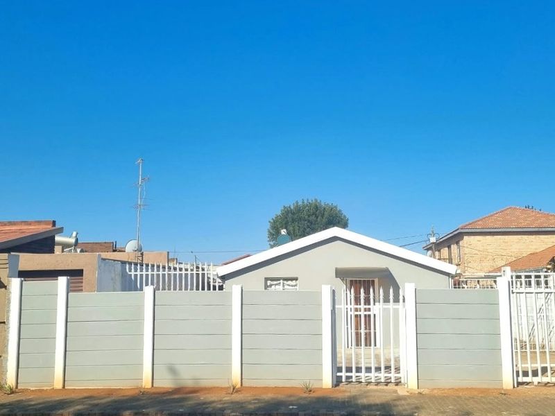 Front view of a residential property featuring a secure boundary wall, gated entrance, and paved driveway area.