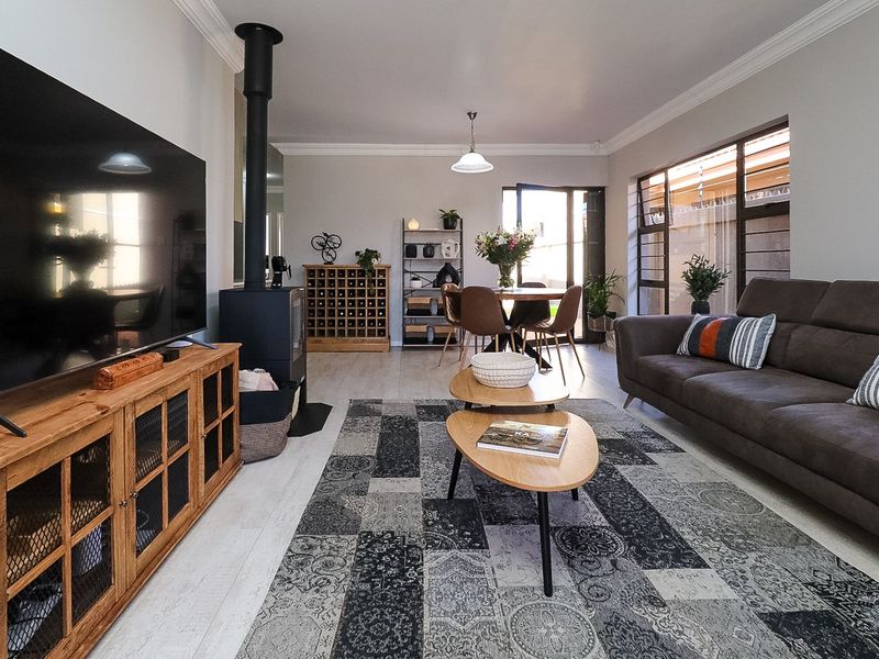 Spacious open-plan living and dining area featuring modern laminate flooring, a freestanding fireplace, and large windows providing natural light.