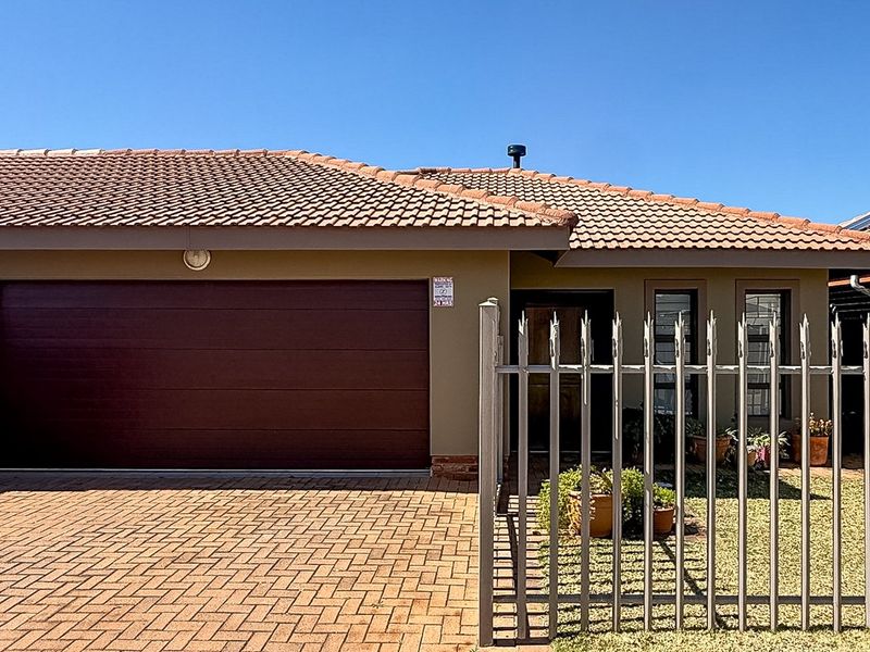Front elevation of a townhouse featuring a tiled roof, a large sectional garage door, and a paved driveway secured by metal fencing.