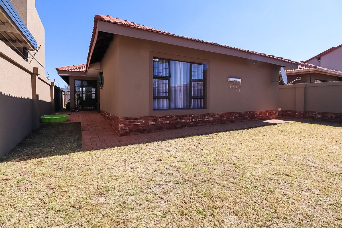Rear view of the townhouse featuring a private garden, paved walkway, and secure window fittings with a terracotta tiled roof.