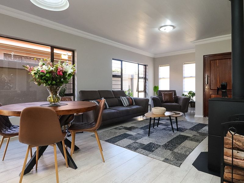 Bright open-plan living and dining area featuring light laminate flooring, a modern wood-burning fireplace, and large windows with security bars.