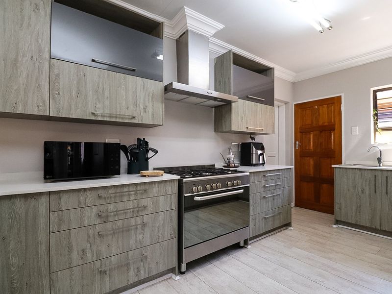 Modern kitchen featuring wood-grain cabinetry, stainless steel gas stove with extractor fan, and light-toned laminate flooring in a well-maintained townhouse setting.