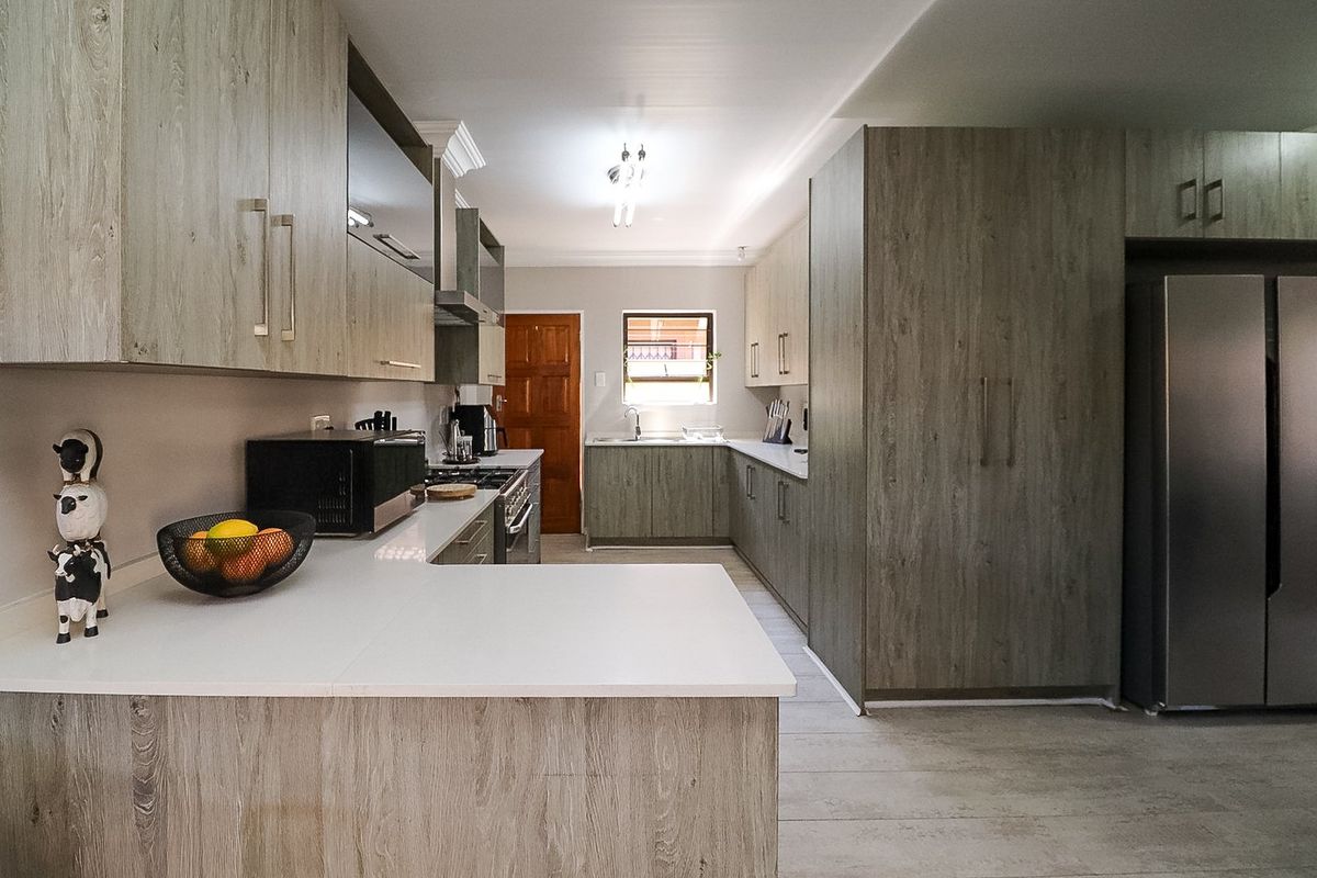 Modern kitchen featuring wood-grain cabinetry, stone countertops, integrated gas hob, extractor fan, and ample storage space with a functional U-shaped layout.