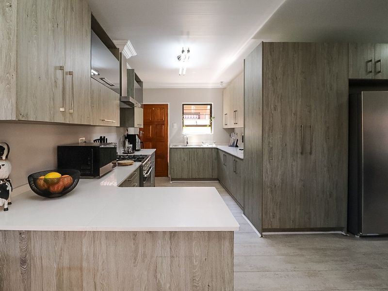 Modern kitchen featuring wood-grain cabinetry, stone countertops, integrated gas hob, extractor fan, and ample storage space with a functional U-shaped layout.