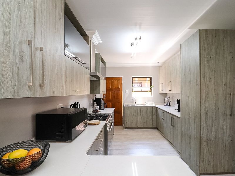 Modern galley-style kitchen featuring light wood-grain cabinetry, stone-look countertops, a gas hob with extractor, and ample storage space.