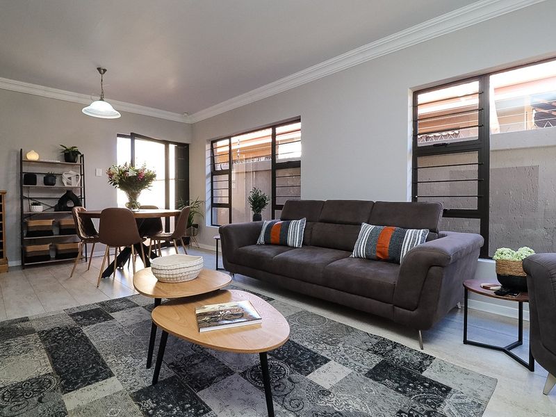 A bright open-plan living and dining area featuring tiled flooring, crown molding, and large louvered windows providing natural light.