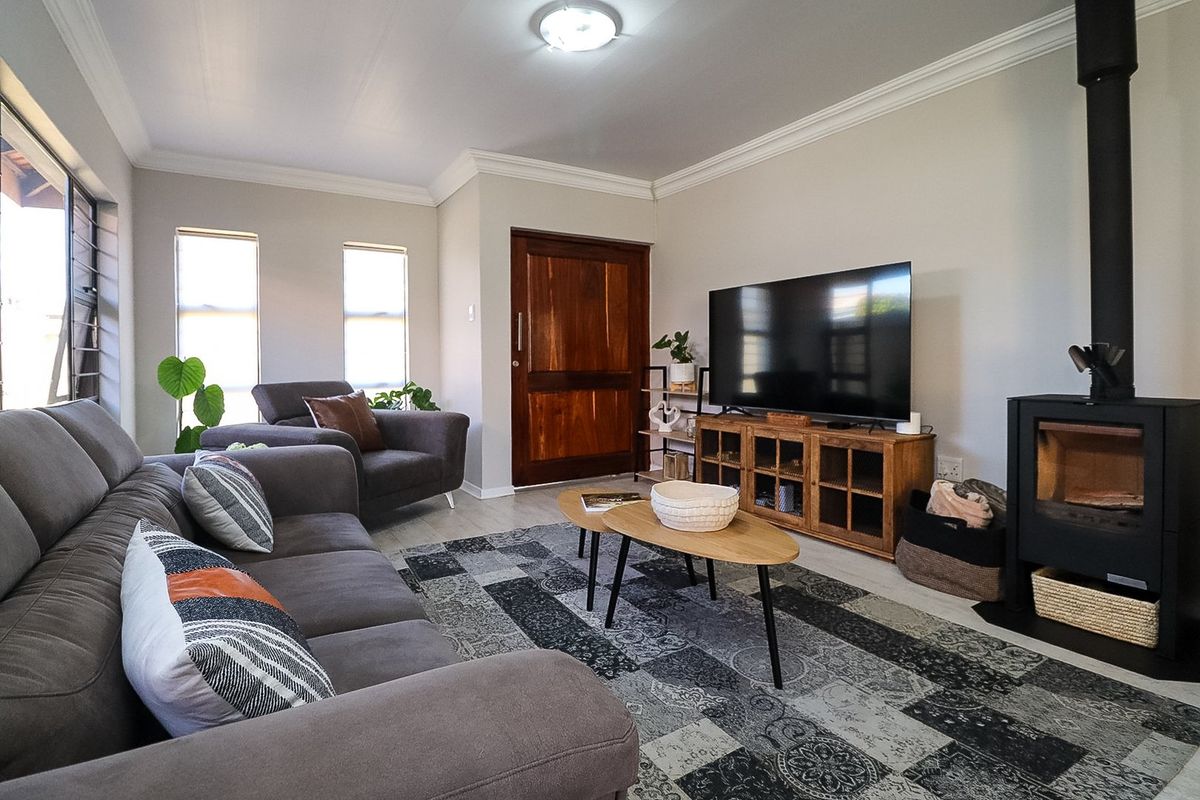 A well-maintained living room featuring a modern wood-burning fireplace, crown molding, and timber entrance door, finished with neutral walls and laminate flooring.