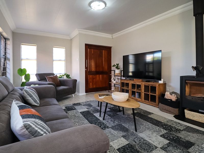 A well-maintained living room featuring a modern wood-burning fireplace, crown molding, and timber entrance door, finished with neutral walls and laminate flooring.