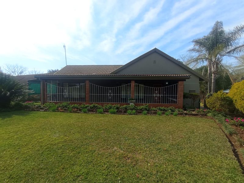 A front view of a single-story house featuring a tiled roof, brick exterior, and a covered patio area overlooking a well-maintained lawn and garden.