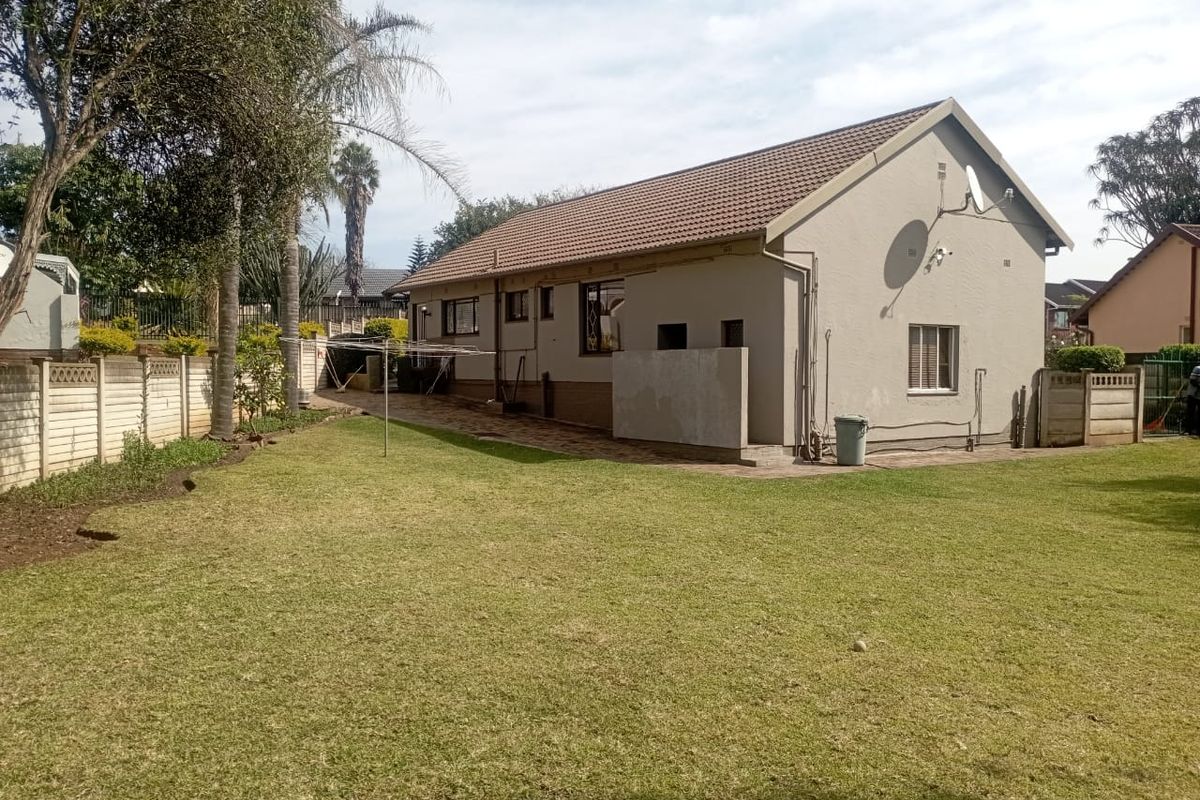 Rear view of the house featuring a spacious lawn, paved walkway, and precast concrete boundary wall.