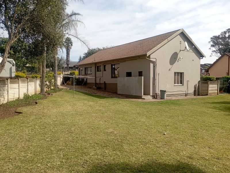 Rear view of the house featuring a spacious lawn, paved walkway, and precast concrete boundary wall.