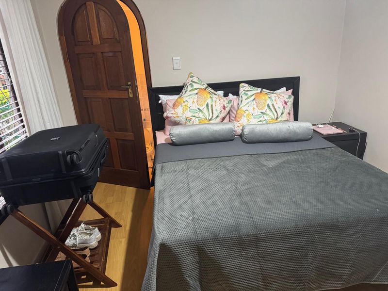A bedroom featuring laminate flooring, an arched wooden door leading to an en-suite, and venetian blinds.