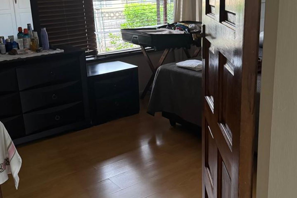 A bedroom featuring laminate flooring, a solid wooden door, and large windows with venetian blinds allowing natural light.