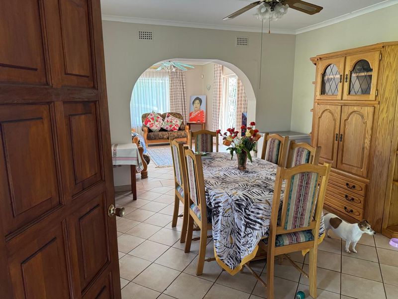 Dining room featuring tiled flooring and a central archway leading to an adjacent living area, with a ceiling fan for climate control.