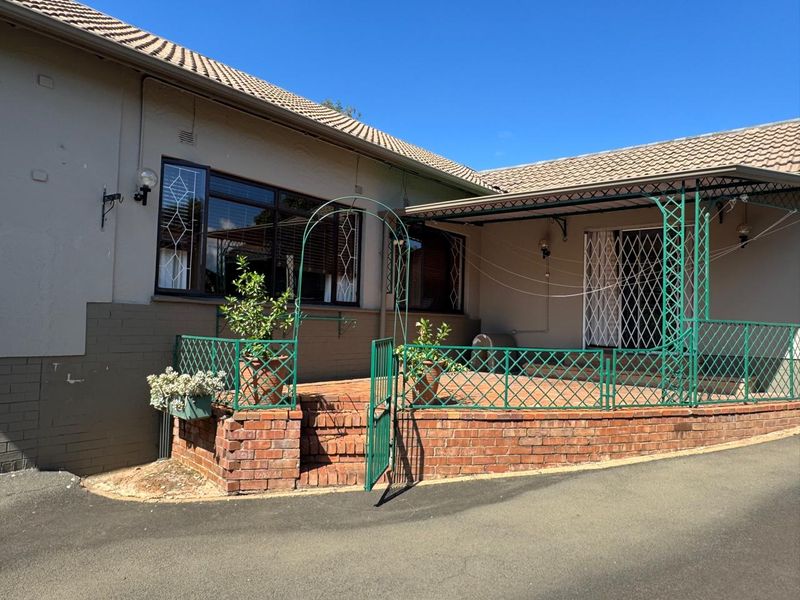 Front exterior view featuring a paved patio area, brick retaining wall, and metal security features including a gate and window bars.