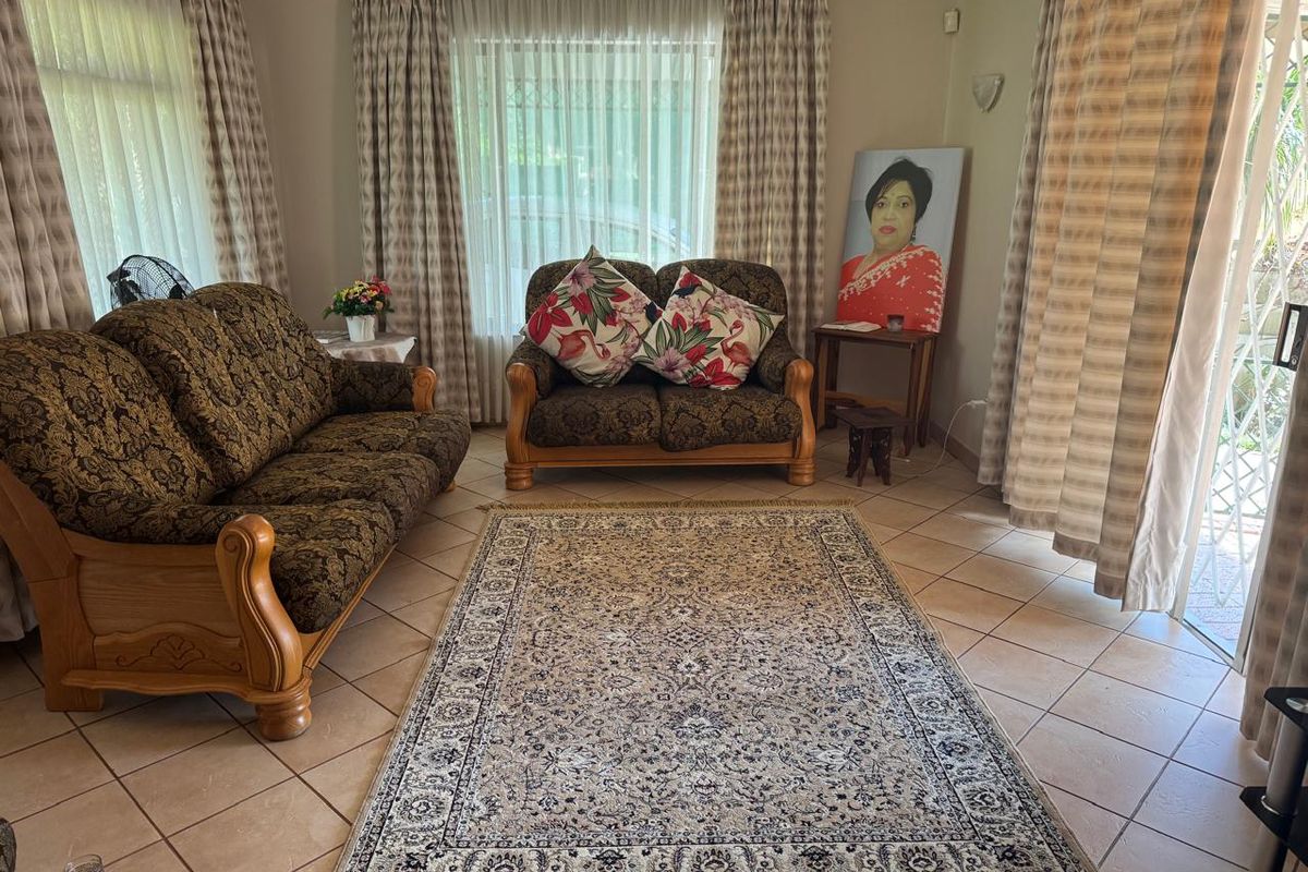 A comfortable living room featuring tiled flooring and large windows with curtain rails, providing access to the outdoor area through a sliding glass door.