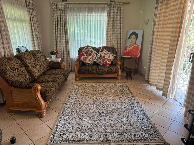 A comfortable living room featuring tiled flooring and large windows with curtain rails, providing access to the outdoor area through a sliding glass door.
