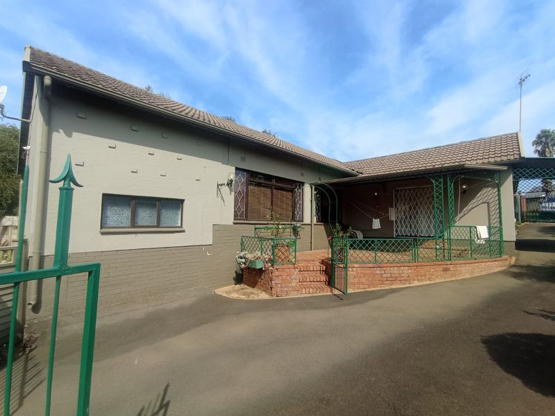 Front exterior view of the house featuring a paved driveway, a raised brick patio area with wrought iron fencing, and security features.