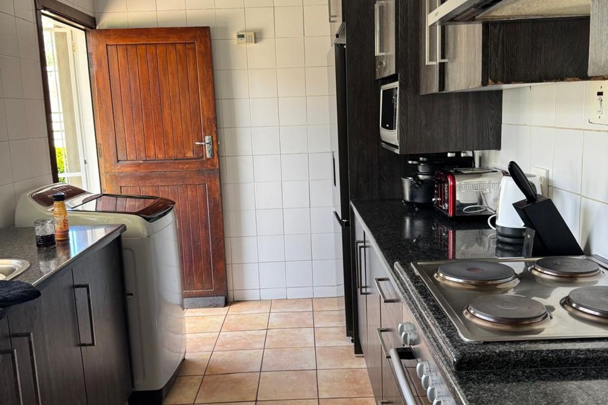 A functional kitchen featuring dark wood cabinetry, granite countertops, an electric hob with extractor, and tiled flooring with direct access to the exterior.
