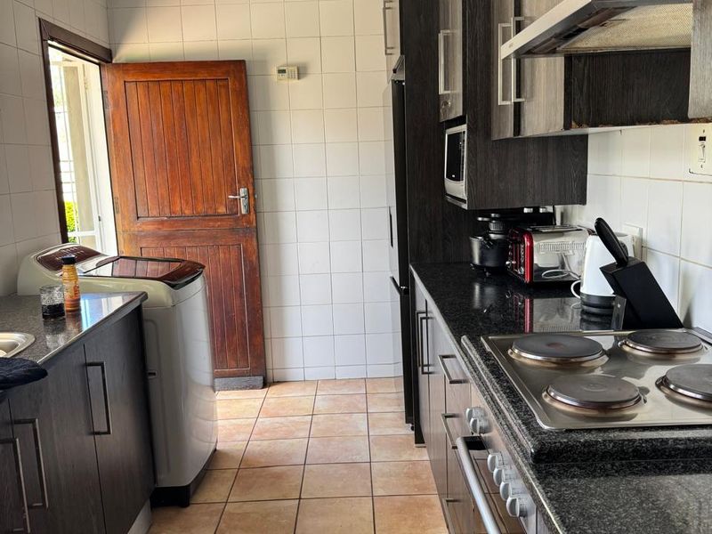 A functional kitchen featuring dark wood cabinetry, granite countertops, an electric hob with extractor, and tiled flooring with direct access to the exterior.