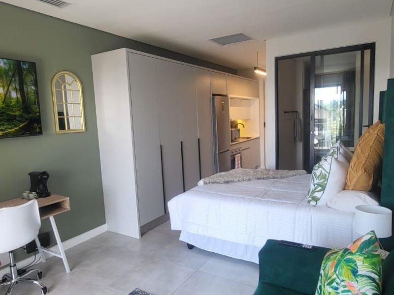 Modern open-plan studio apartment featuring sleek built-in cabinetry, tiled flooring, and seamless access to a private balcony through sliding glass doors.