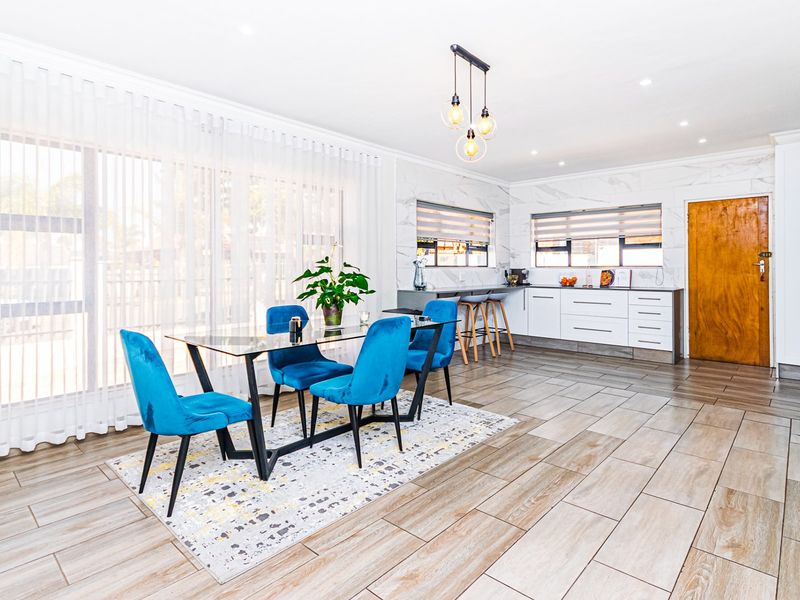 Modern open-plan living and kitchen area featuring marble-look wall finishes, sleek white cabinetry, a breakfast bar, and large sliding doors for natural light.