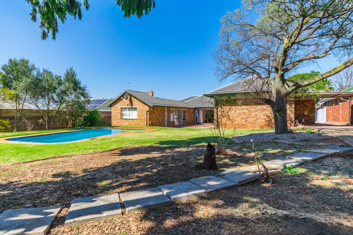 Spacious rear garden featuring a swimming pool, established trees, brick exterior facade, and a paved walkway leading to the main house.