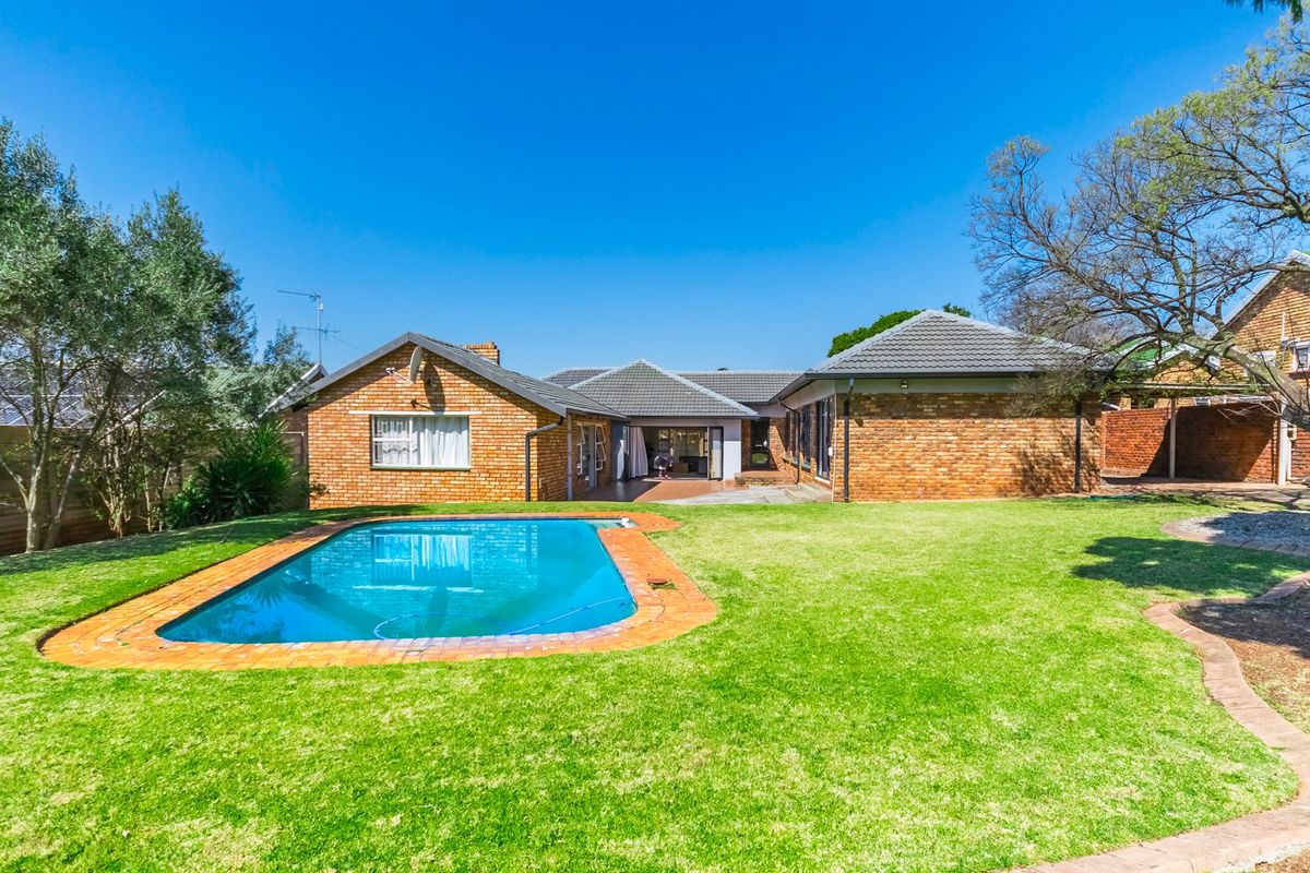 Rear view of the property featuring a well-maintained brick house, a swimming pool with paved surround, and a spacious green lawn.
