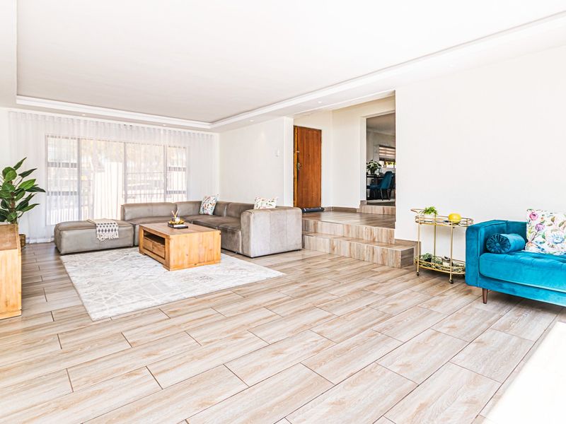 Spacious living room featuring modern wood-look tile flooring, recessed lighting, and a raised platform area leading to an adjacent room.