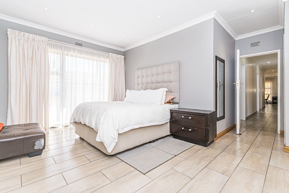 A well-lit bedroom featuring neutral grey walls, tiled flooring, and a sliding glass door providing natural light.