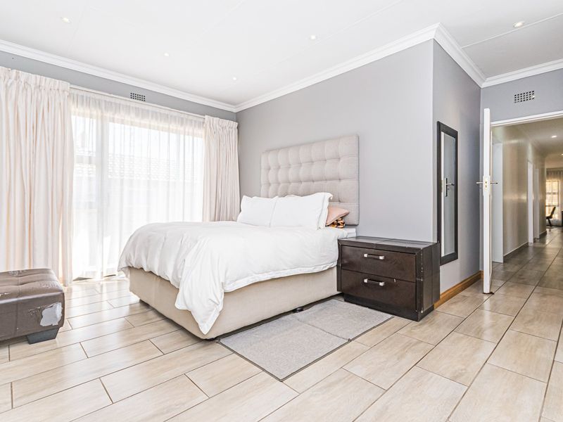 A well-lit bedroom featuring neutral grey walls, tiled flooring, and a sliding glass door providing natural light.