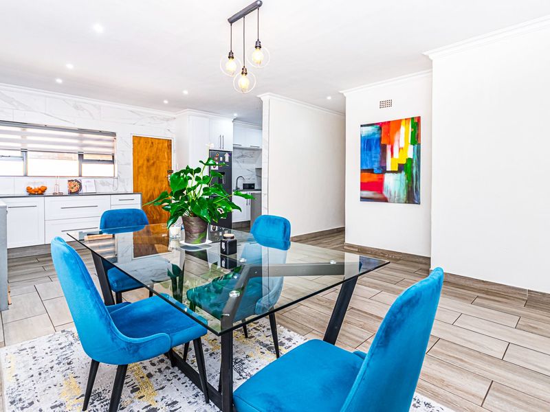 An open-plan dining and kitchen area featuring modern tiled flooring, marble-look wall accents, and contemporary pendant lighting.